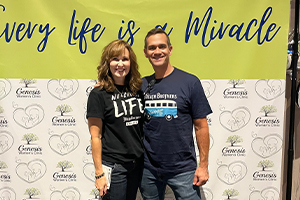 Wendy Burpee and man standing inf ront of Life is a Miracle banner.