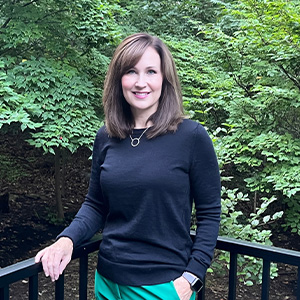 Wendy Burpee standing along black fence with trees in background.